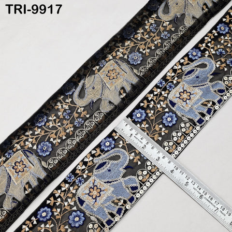 a decorative fabric with a repeating pattern of elephants and flowers in shades of blue and gold. The fabric appears to be a decorative trim or border, with a ruler placed on it to provide a size reference.