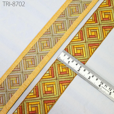 a close-up view of a decorative fabric with a repeating geometric pattern in shades of yellow, orange, and red. A ruler is placed next to the fabric, indicating its size or dimensions.