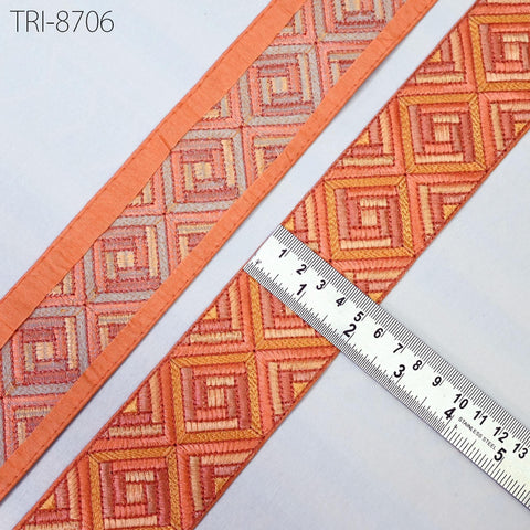 a close-up view of a decorative fabric with a geometric pattern in shades of orange and red. A ruler is placed next to the fabric, indicating its size.