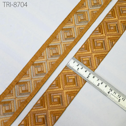 two pieces of gold-colored fabric with a geometric pattern, placed next to a ruler for size comparison.