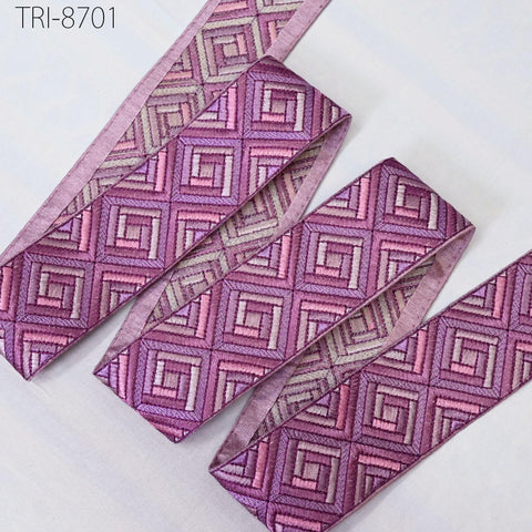 a collection of decorative fabric pieces with a geometric pattern in shades of purple and pink. The fabric appears to be made of a shiny material and is arranged in a way that suggests it is being used for embellishment or as a decorative element.