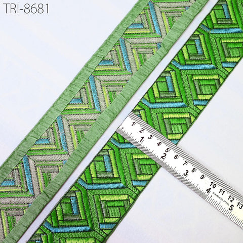 a close-up view of a decorative green and blue embroidered fabric, with a ruler placed next to it to measure its dimensions.