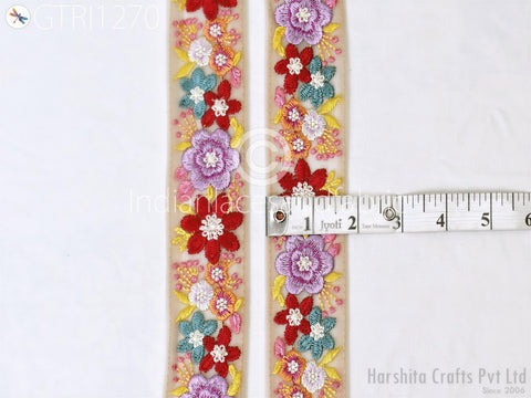 a decorative floral embroidery on a beige background, with a ruler placed next to it to measure the length of the embroidery.