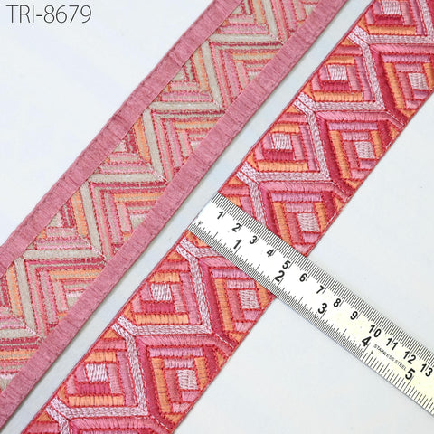 two pieces of fabric with a geometric pattern in shades of pink and orange, placed next to a ruler for size comparison.
