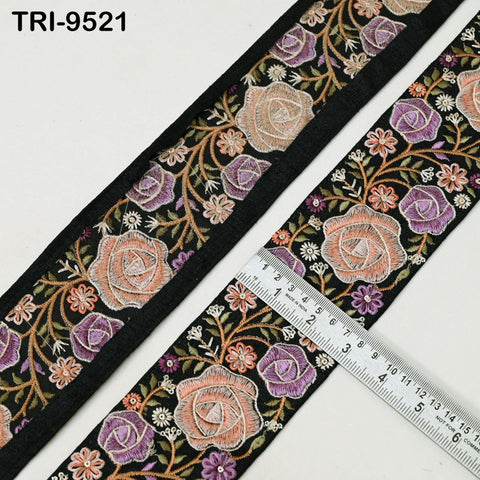 a decorative fabric with a floral pattern, including roses and other flowers in shades of purple, orange, and white. The fabric is black and has a black border. A ruler is placed on the fabric, indicating the size or dimensions of the pattern.
