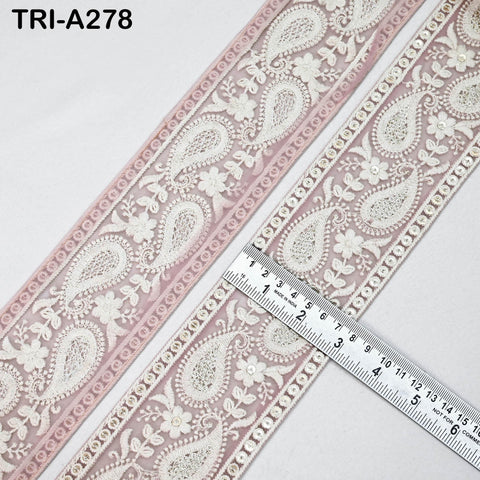a close-up view of a decorative fabric with a repeating paisley pattern in shades of pink and white. A ruler is placed next to the fabric, indicating the size of the pattern.