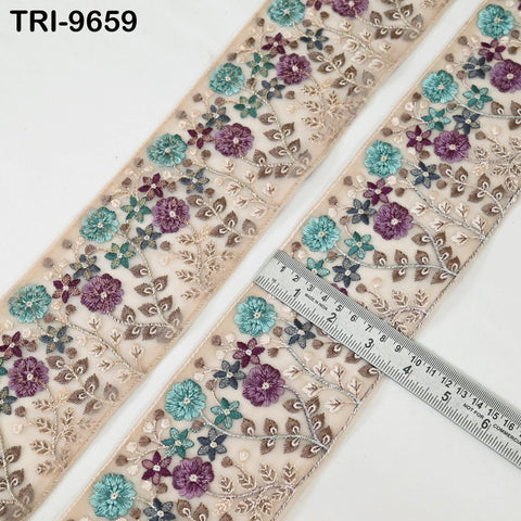 two pieces of fabric with a floral embroidered design in shades of purple, blue, and green. A ruler is placed on top of the fabric, indicating the size of the fabric pieces.