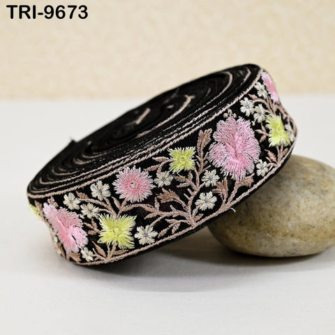 A black and pink embroidered ribbon with a floral pattern is displayed on a white surface, resting on a rock.