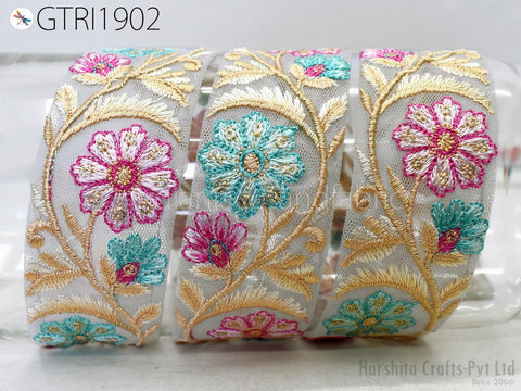 a close-up view of a decorative fabric with a floral pattern. The fabric is adorned with three distinct flower designs, each with a unique color scheme. The flowers are arranged in a circular pattern, creating a visually appealing and intricate design. The fabric appears to be made of a light-colored material, which complements the vibrant colors of the flowers. The image does not contain any text or other objects, and the focus is solely on the floral design.
