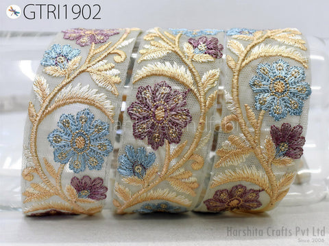 a close-up view of a decorative fabric with intricate floral embroidery in shades of blue, purple, and gold. The fabric appears to be a piece of jewelry or a decorative accessory, with the floral patterns and gold accents creating a visually appealing and elegant design.