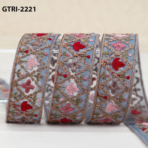 A close-up image of a decorative ribbon with intricate floral embroidery in shades of blue, pink, and red.
