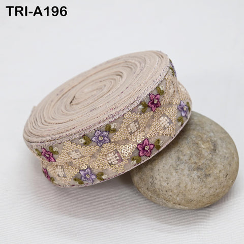 a decorative beige fabric with a floral pattern, including purple and green flowers, rolled up and placed on a gray rock.