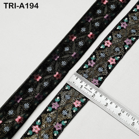 a close-up view of a decorative black ribbon with a floral pattern. A ruler is placed on the ribbon, indicating its size.