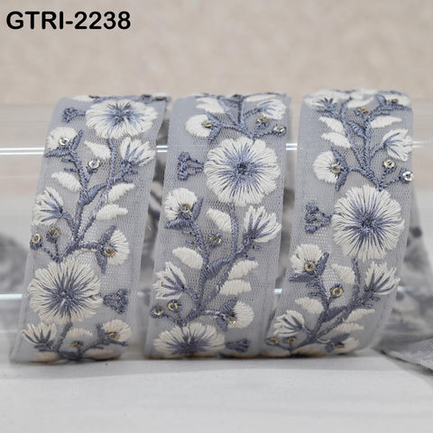 A close-up image of a decorative fabric with a floral pattern in shades of gray and white, featuring small flowers and leaves.