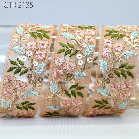 three decorative fabric pieces with intricate floral embroidery in shades of pink, green, and beige. The pieces appear to be made of a light-colored material, possibly lace or fabric.
