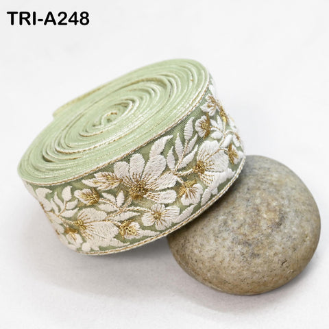 a green and white floral embroidered ribbon and a gray rock, both resting on a white surface.