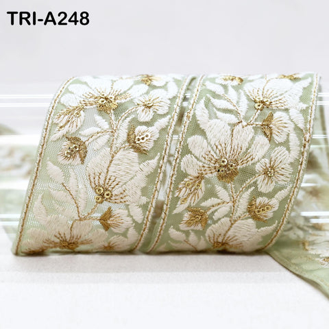 a decorative fabric with a floral pattern, featuring white and gold embroidered flowers on a green background.