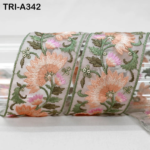 a decorative fabric with a floral pattern, including pink and green flowers, leaves, and other floral elements. The fabric appears to be a ribbon or a piece of cloth with a floral motif.