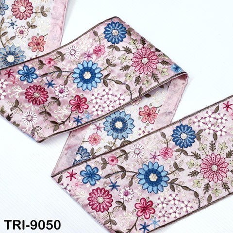 a close-up view of a decorative fabric with a floral pattern in shades of pink, blue, and white. The fabric appears to be a decorative trim or ribbon, with the pattern of flowers and leaves visible on the surface.