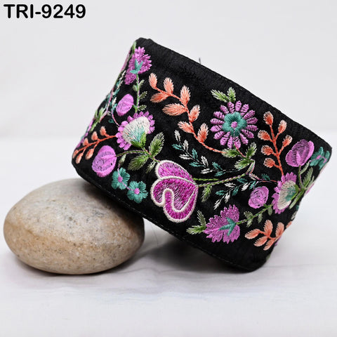 a black fabric with a floral pattern, including purple, pink, and green flowers, as well as green leaves, arranged in a decorative manner.