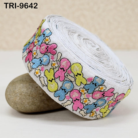 A roll of colorful, embroidered fabric with a playful design of cartoon-like characters on it, placed on a surface next to a rock.
