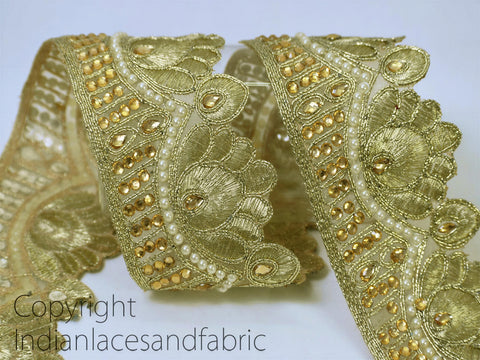 a close-up view of a decorative gold-colored fabric with intricate floral and leaf-like patterns, as well as numerous small gold beads or pearls scattered throughout the fabric.