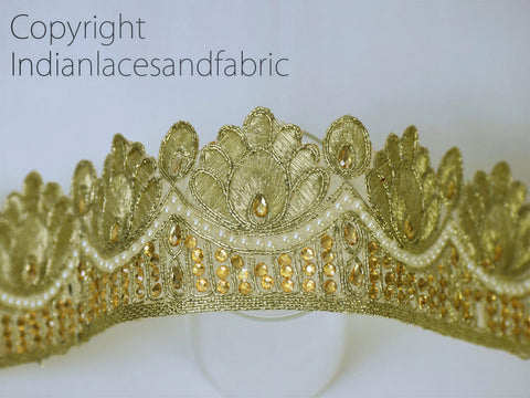 A close-up view of an ornate gold-colored crown or headdress with intricate embroidery and embellishments, including small pearls and gemstones.