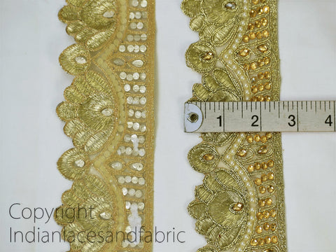 two pieces of gold embroidered fabric with intricate designs, including flowers and beads. A ruler is placed between the two pieces of fabric to measure their length.