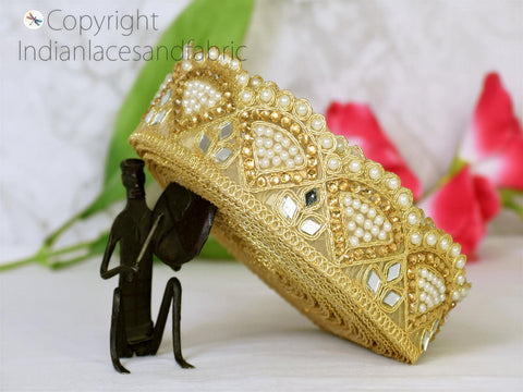 a gold crown adorned with pearls and intricate designs, placed on a white surface. A small black figurine is positioned next to the crown, creating a visually striking contrast.