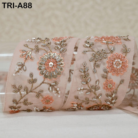 a decorative fabric with intricate floral and leaf designs, featuring a combination of pink and gold colors. The fabric appears to be a piece of lace or a similar type of material, with a floral pattern and embellishments such as beads or sequins.