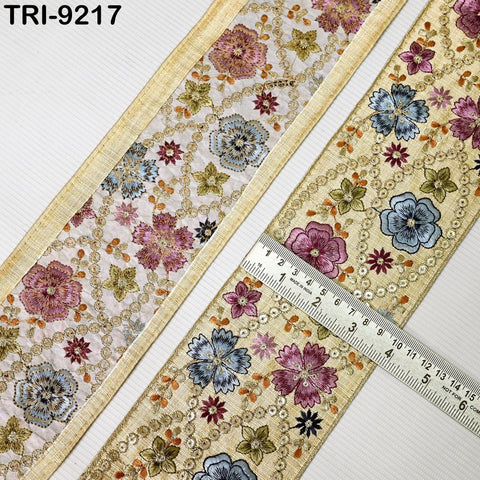 two pieces of fabric with intricate floral designs, including pink, blue, and yellow flowers, as well as other decorative elements. A ruler is placed on the fabric, indicating the size or dimensions of the floral patterns.