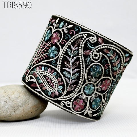 a decorative black and white fabric with a paisley pattern, adorned with colorful flowers and leaves. The fabric is placed on a white surface, with a rock nearby.