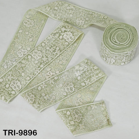 a roll of green lace ribbon with a floral pattern, lying on a white surface.