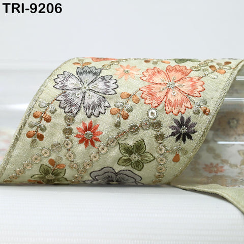 a decorative fabric with a floral pattern, including various shades of green, orange, and purple flowers. The fabric appears to be a ribbon or a piece of cloth with a floral design.