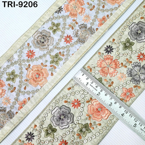 a close-up view of a decorative fabric with a floral pattern. The fabric is adorned with a variety of colorful flowers, including red, orange, and green ones, arranged in a repeating pattern. A ruler is placed on the fabric, likely for measuring purposes. The image does not contain any text, and the focus is on the intricate floral design and the ruler for size reference.