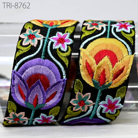 two decorative fabric pieces with vibrant floral patterns. The left piece is a black fabric with a purple and red floral design, while the right piece is a yellow fabric with a red and orange floral design. Both pieces are adorned with numerous small flowers and leaves, creating a visually striking and intricate appearance.