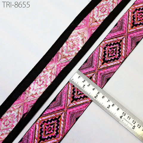 a close-up view of a decorative fabric with a pink and black geometric pattern, placed next to a ruler for size reference.