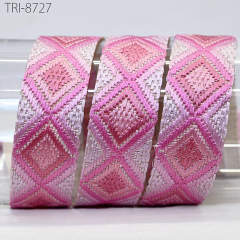 A roll of pink and white embroidered ribbon with a diamond pattern, arranged in a row.