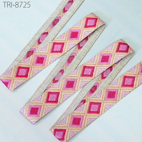 several spools of colorful, patterned fabric with diamond-shaped designs in shades of pink, beige, and peach.