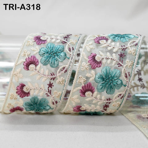 two pieces of fabric with intricate floral embroidery in shades of blue and purple. The fabric appears to be a decorative trim or ribbon, with the floral patterns visible on both pieces.