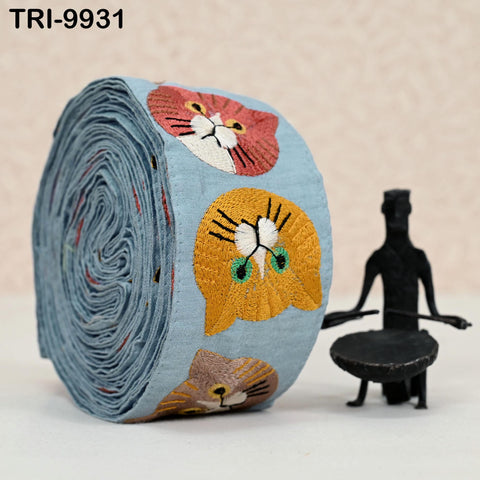 a blue fabric with cat embroidery, including two cat faces, and a small black figurine of a person playing a drum.