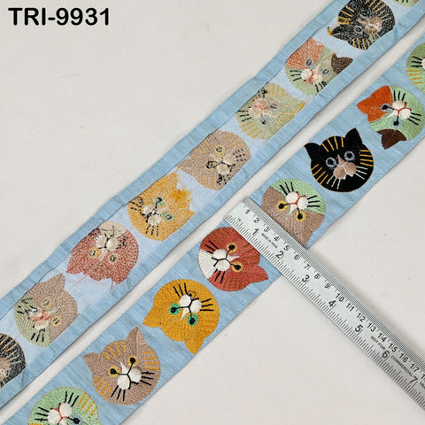 a blue fabric with a repeating pattern of cat faces, including various shades of orange, yellow, and black cats. A ruler is placed next to the fabric, likely for measuring the length or width of the fabric.