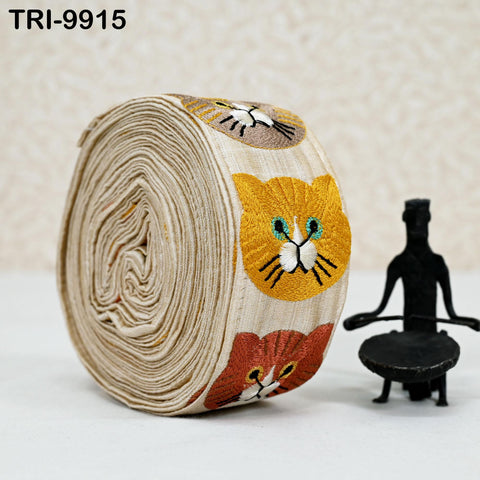 A large roll of fabric with cat embroidery, and a small black figurine next to it.