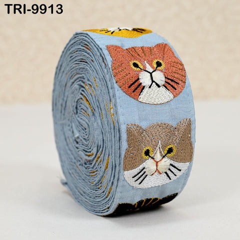 A blue spool of thread with two cat embroidered faces on it.