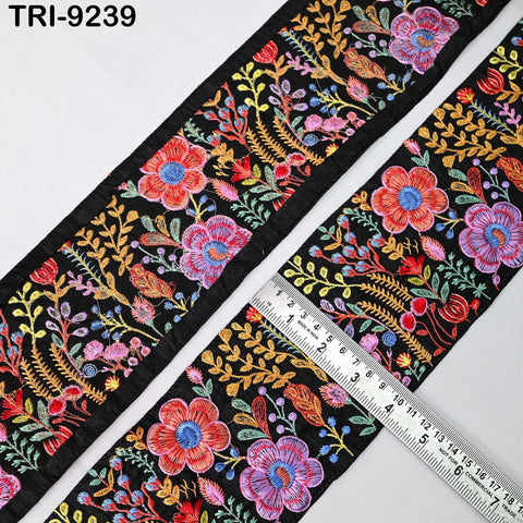 a close-up view of a decorative fabric with a floral pattern. The fabric is black and features a variety of colorful flowers and leaves in shades of red, pink, blue, and yellow. A ruler is placed on the fabric, likely for measuring purposes.