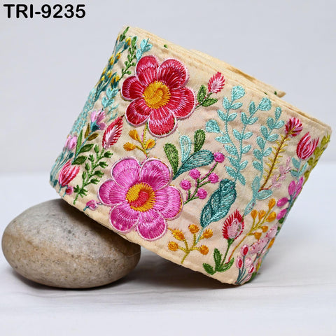 a decorative fabric with a floral pattern, including pink and red flowers, green leaves, and other colorful elements. The fabric is folded and placed on a rock, creating an aesthetically pleasing composition.