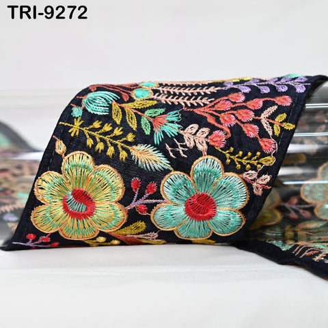a close-up view of a decorative fabric with a floral pattern. The fabric is predominantly black, adorned with colorful flowers and leaves in shades of green, red, and yellow. The image is a close-up of the fabric, showcasing the intricate details and vibrant colors of the embroidered design.