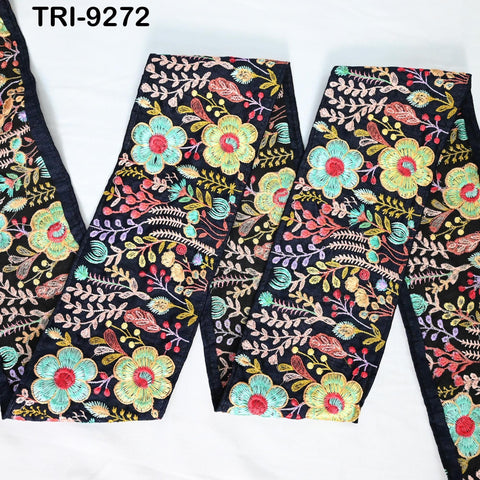 a close-up view of a fabric with a floral pattern in various colors, including green, red, and yellow flowers. The fabric appears to be a piece of embroidered material, possibly a scarf or a garment.
