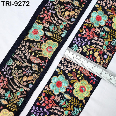 a close-up view of a decorative fabric with a floral pattern. The fabric is black and features a variety of colorful flowers and leaves, creating a vibrant and intricate design. A ruler is placed on the fabric, likely for measuring purposes.