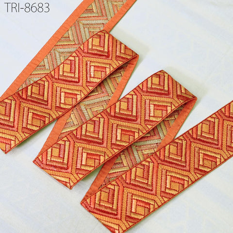 a collection of decorative fabric pieces with a geometric pattern in shades of orange and red. The fabric appears to be a type of ribbon or textile, with a repeating pattern of interlocking shapes. The image does not contain any text or other discernible objects, and the focus is on the intricate design and color of the fabric.